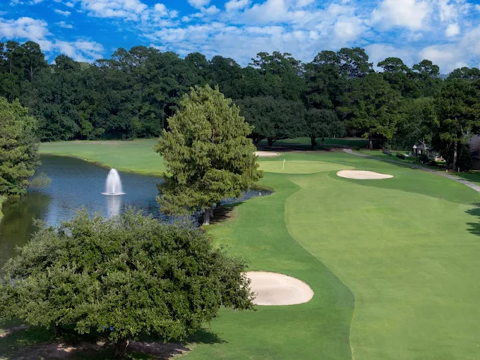 April Sound Golf Club course with green fields, a water fountain, trees and blue skies.