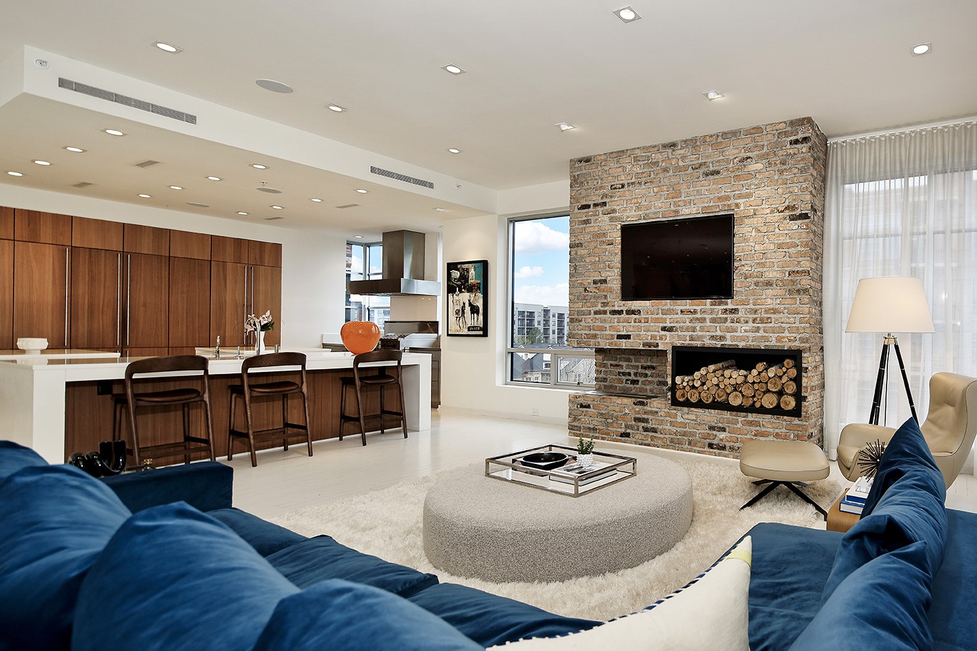 Interior view of a luxury condominium with a kitchen bar, fireplace, and views of The Woodlands from the window.