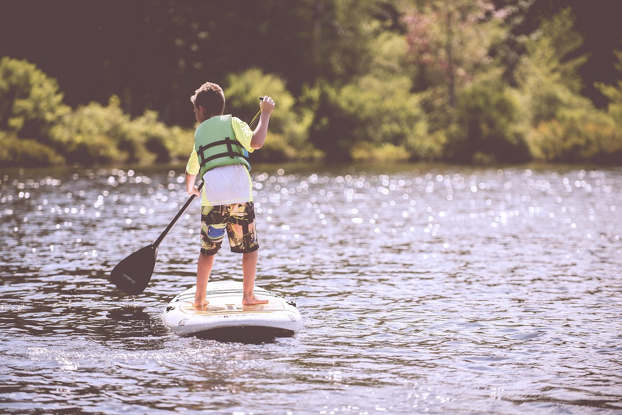 Photographic image of a young boy paddleboarding on a lake.
